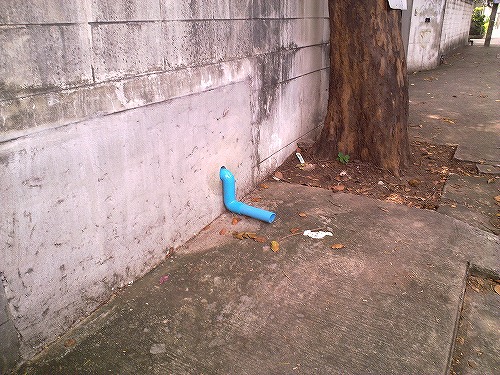 高い位置から突き出たパイプ。塀に穴を開けて通しています