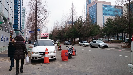 テジョンの一方通行の道にある、とある路上駐車場。左側車両辺りに座っているのが管理人、道路の右側１列が駐車場