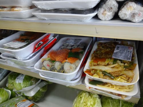 日本食品を取り扱う店で販売されている弁当の近くで陳列されている寿司パック（海苔巻き、サーモンの刺身、にぎり寿司、ホットロール入り）やヤキソバパック