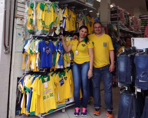 ブラジルカラーの服が並ぶ子供用品店と、ブラジルカラーの服を着た店員さん