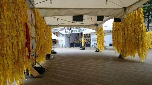 特設テントの脚がリボンで埋められ、奥には献花台が見える