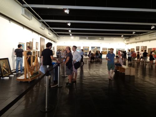 作品の取り付けが行われる展示会場で絵画鑑賞する人々