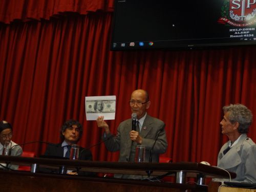 現在のアメリカの100ドル紙幣のコピーを片手に講演する菊池さん