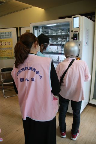 購入の様子を見つめるピンクのベストを着たボランティアスタッフ