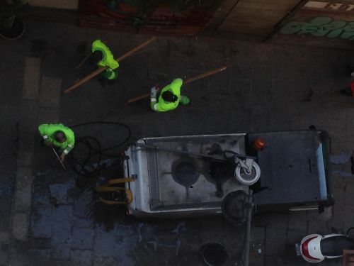 地面の排水管から水の補給をしている清掃車と清掃人